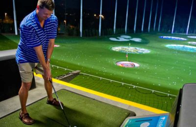 A man in shorts about to take a swing at a golf ball at Topgolf