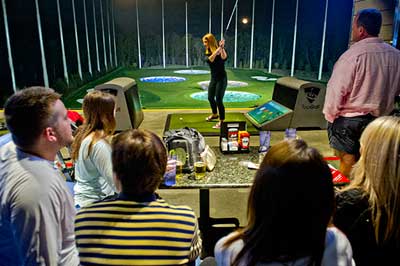 a group of friends watches someone taking a swing at Topgolf