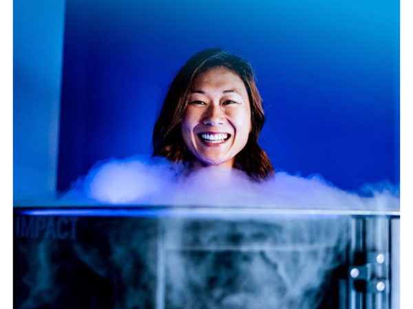 A woman smiling standing behind a large Cryotherapy tank