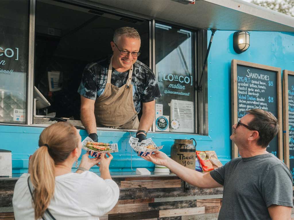vendor handing food to people at food truck alley