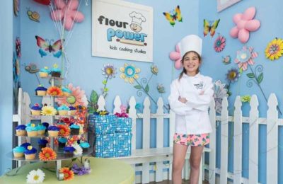 girl with chef hat standing by cupcakes