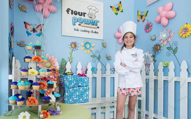 girl with chef hat standing by cupcakes