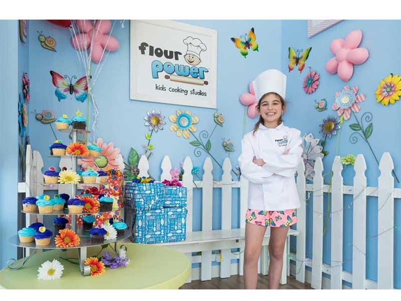 girl with chef hat standing by cupcakes