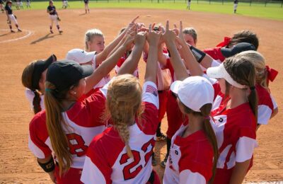 softball team in huddle with hands in air