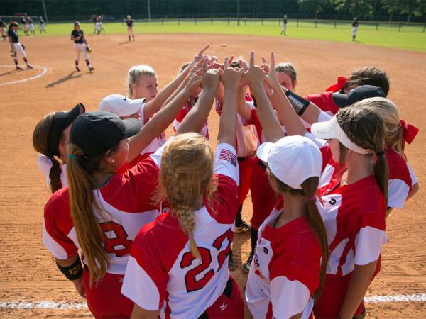 softball team in huddle with hands in air